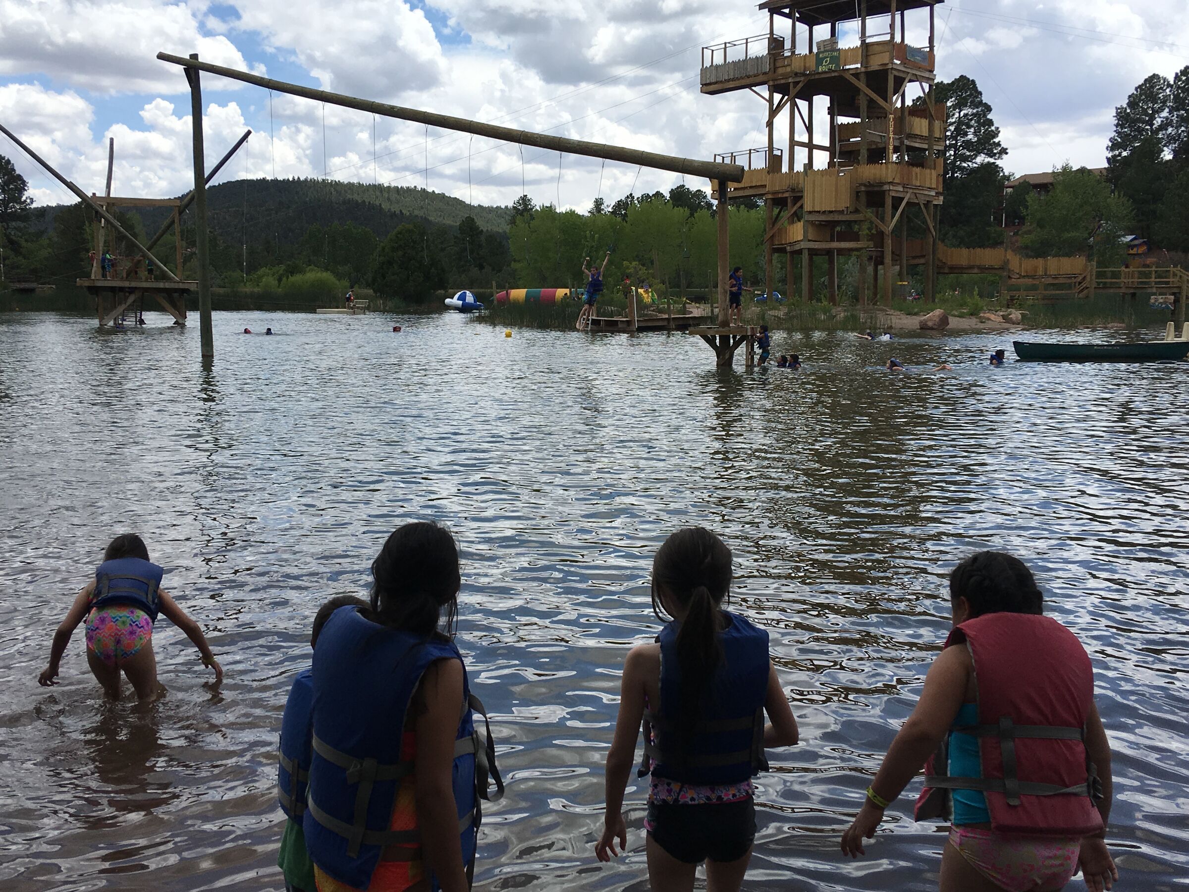 Niños con chalecos salvavidas entran al lago en Glorieta, vistos de espaldas.