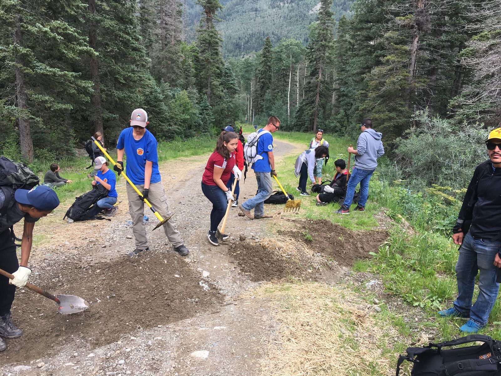 Kids with shovels and rakes dig a drainage across a gravel forest road.