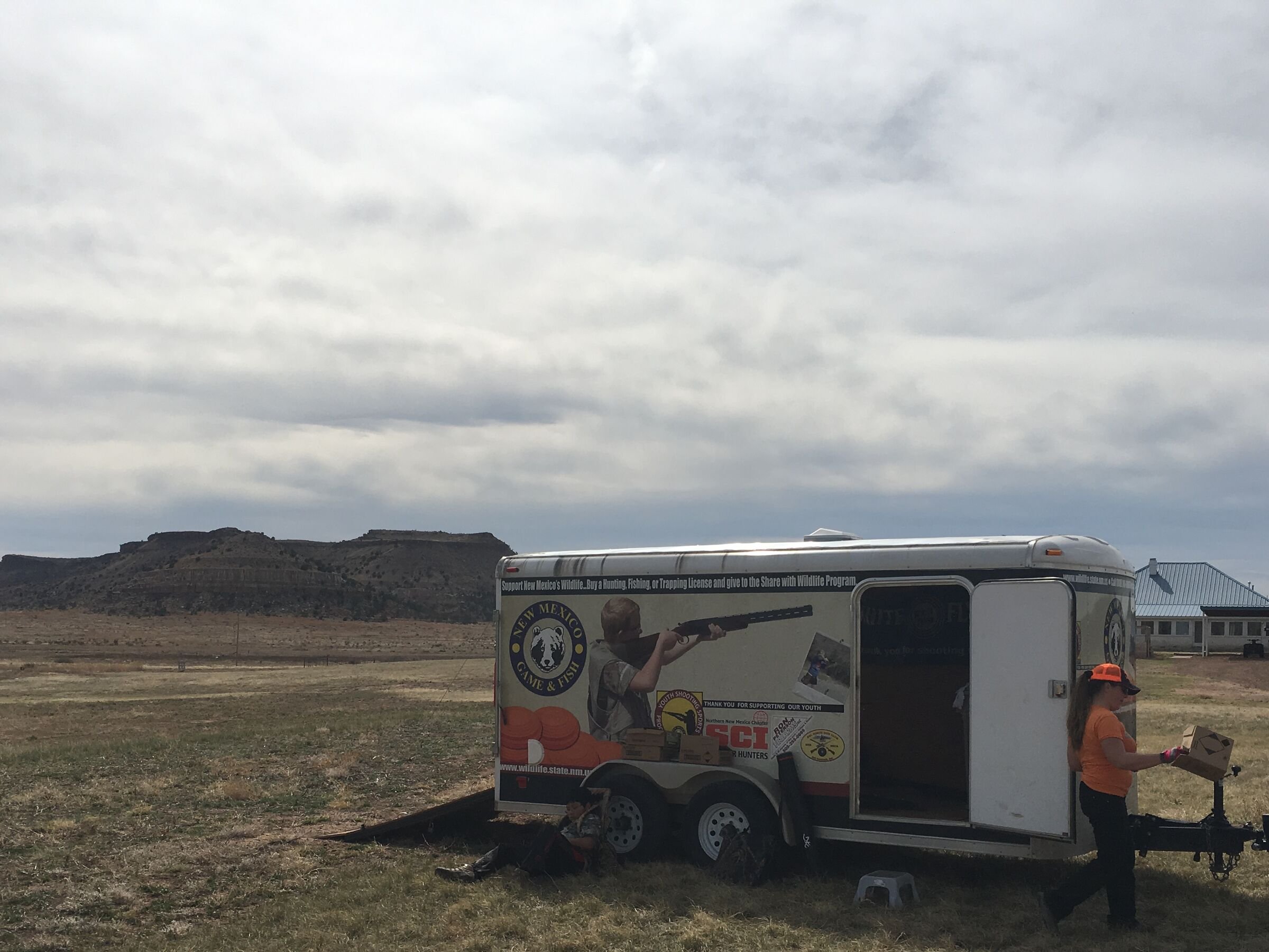 The camp trailer parked on open plains under a grey sky, a mesa behind.